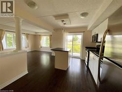Open-concept living space featuring dark wood-finish flooring, a kitchen island with a dark countertop, white kitchen cabinetry with stainless steel appliances, and a sliding glass door leading to a b - 
