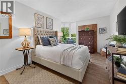 Bright sleeping area featuring wood-finish flooring, white walls, and a large bay window - 