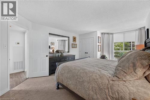 Carpeted bedroom featuring a large window with white blinds and sheer drapes, a closet with bifold doors, and an entryway with wood-finish flooring - 1237 North Shore Boulevard Unit# 405, Burlington, ON - Indoor Photo Showing Bedroom