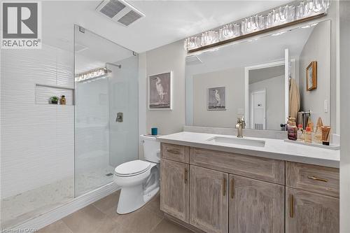 Spacious bathroom featuring a glass-enclosed shower with white textured tile, a built-in shower niche, and a vanity with a light wood-finish double cabinet and a single rectangular undermount sink - 1237 North Shore Boulevard Unit# 405, Burlington, ON - Indoor Photo Showing Bathroom