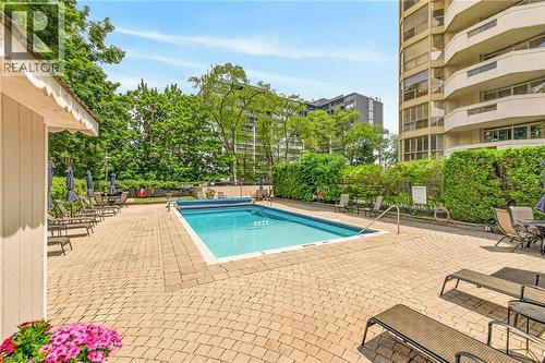 Outdoor swimming pool surrounded by a large paver patio, lush perimeter landscaping, and mature trees - 1237 North Shore Boulevard Unit# 405, Burlington, ON - Outdoor With In Ground Pool