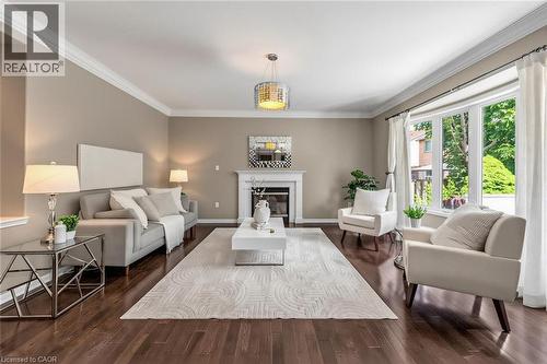 Spacious living area featuring rich wood-finish flooring, a prominent fireplace with a white mantle, a large bay window, crown molding, and a modern chandelier - 729 Boughton Crescent, Milton, ON 