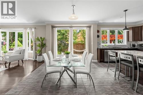 Open-concept living space featuring a dining area with a glass-top table, a kitchen with dark cabinetry and a stone countertop, and a living area with large bay windows - 729 Boughton Crescent, Milton, ON 