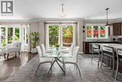 Open-concept living space featuring a dining area with a glass-top table, a kitchen with dark cabinetry and a stone countertop, and a living area with large bay windows - 