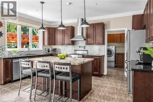 Spacious kitchen featuring an island with a stone countertop, dark wood-finish cabinetry, stainless steel appliances, and a mosaic tile backsplash - 729 Boughton Crescent, Milton, ON 