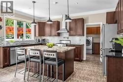 Spacious kitchen featuring an island with a stone countertop, dark wood-finish cabinetry, stainless steel appliances, and a mosaic tile backsplash - 