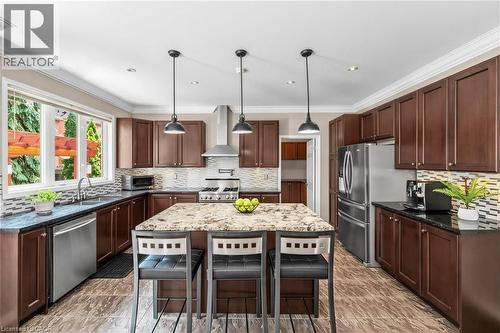 Kitchen featuring an island with stone countertop, stainless steel appliances, dark wood cabinetry, tile backsplash, and wood-finish flooring - 729 Boughton Crescent, Milton, ON 