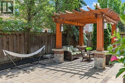 Expansive paver patio featuring a wooden pergola with stone-clad pillars and integrated lighting - 729 Boughton Crescent, Milton, ON 