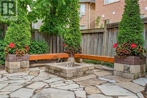Stone patio featuring a fire pit, integrated wooden benches, and decorative planters - 729 Boughton Crescent, Milton, ON 