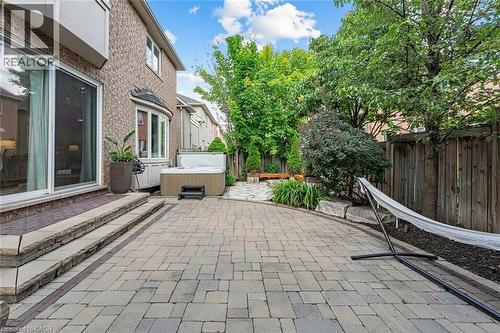 Expansive stone paver patio featuring a built-in hot tub, mature trees, and a wooden fence - 729 Boughton Crescent, Milton, ON 