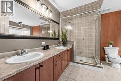 Bathroom featuring a dual vanity with undermount sinks, a glass-enclosed shower with subway tile surround, a built-in toilet, and an accent wall with vertical wood paneling - 