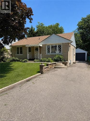 Brick exterior with a peaked roofline, front lawn, stone retaining wall, and an attached garage - 355 East 36Th Street, Hamilton, ON 