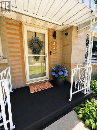 Covered front porch featuring a glass-paneled storm door, brick facade, white metal railing, and overhead lighting - 355 East 36Th Street, Hamilton, ON 