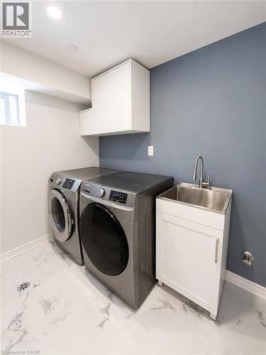Dedicated laundry area featuring modern appliances, white cabinetry, a utility sink with a chrome faucet, and white marble-look flooring - 355 East 36Th Street, Hamilton, ON 