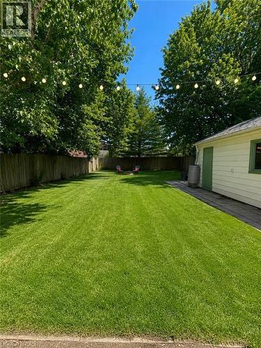 Expansive backyard featuring a lush lawn, mature trees providing natural canopy, string lighting, and a wood privacy fence - 355 East 36Th Street, Hamilton, ON 