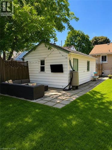 Backyard featuring a white horizontal siding structure with a green shingled roof, a square paver patio, and a grass lawn - 355 East 36Th Street, Hamilton, ON 