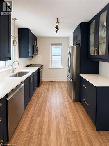Galley kitchen featuring dark blue cabinetry, light wood-finish flooring, and white countertops - 355 East 36Th Street, Hamilton, ON 