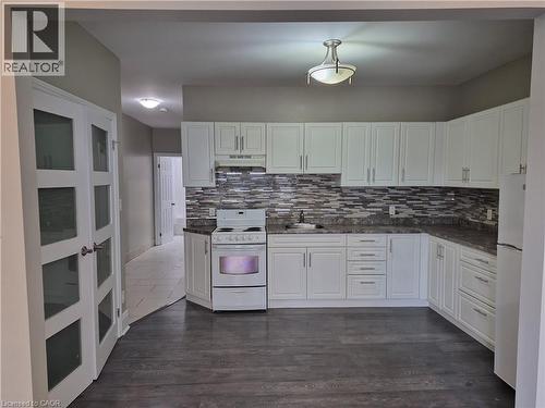 Kitchen featuring white cabinetry, a mosaic tile backsplash, dark countertops, and wood-finish flooring - 181 King Street E Unit# 2, Kitchener, ON 