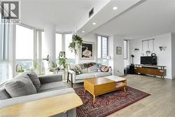 Expansive living area featuring light wood-finish flooring, a contemporary ceiling with recessed lighting, and a prominent bay window wall offering abundant natural light - 
