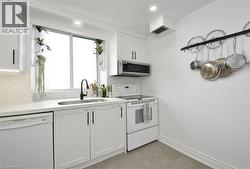 Bright kitchen featuring white cabinetry, a built-in microwave, a stainless steel sink with a matte black faucet, a white dishwasher, and light-colored countertops with a matching backsplash - 