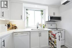 Kitchen featuring white cabinetry with black hardware, white speckled countertops, an undermount sink with a black faucet, and a stainless steel over-the-range microwave - 