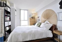 Bright bedroom featuring a large window, white walls, and wood-finish flooring - 