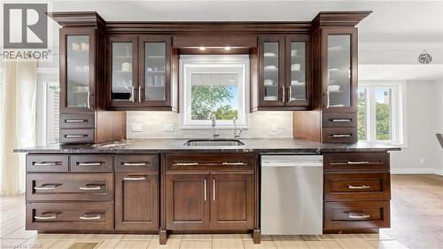 Rich wood-finish cabinetry featuring glass-front uppers, an undermount sink, a stainless steel dishwasher, and dark stone countertops - 438 Lexington Road, Waterloo, ON 