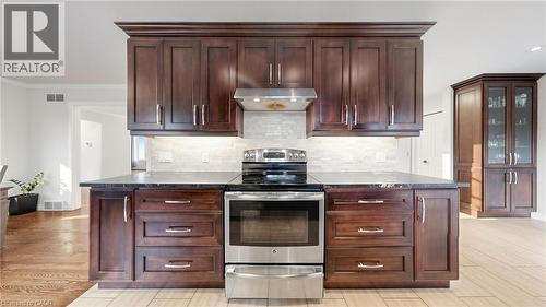 Kitchen featuring dark wood cabinetry, stainless steel range and range hood, black countertops, and a light-toned backsplash - 438 Lexington Road, Waterloo, ON 