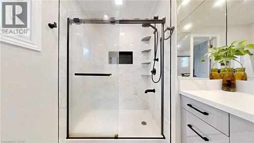 Shower enclosure featuring a sliding glass door with dark bronze framing, white tiled walls with subtle veining, multiple built-in shelving units, and a rainfall showerhead - 438 Lexington Road, Waterloo, ON 