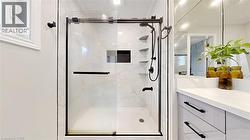 Shower enclosure featuring a sliding glass door with dark bronze framing, white tiled walls with subtle veining, multiple built-in shelving units, and a rainfall showerhead - 