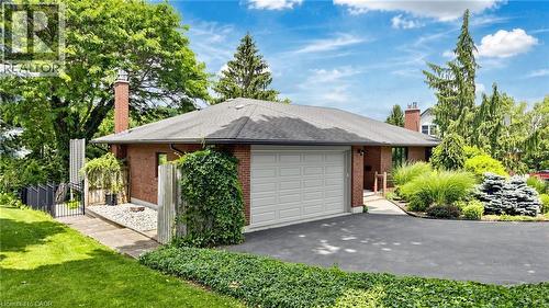 Brick exterior featuring an attached two-car garage, asphalt driveway, mature landscaping, and a side patio with a metal gate - 438 Lexington Road, Waterloo, ON 