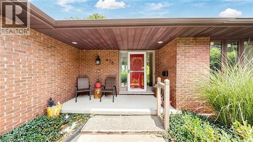 Brick exterior featuring a covered porch with concrete flooring, recessed lighting, and a prominent red front door - 438 Lexington Road, Waterloo, ON 