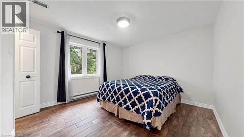 Bedroom featuring wood-finish flooring, white baseboards, a white paneled door with dark hardware, a rectangular window, and a flush-mount ceiling light - 438 Lexington Road, Waterloo, ON 