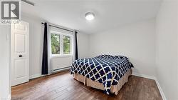 Bedroom featuring wood-finish flooring, white baseboards, a white paneled door with dark hardware, a rectangular window, and a flush-mount ceiling light - 