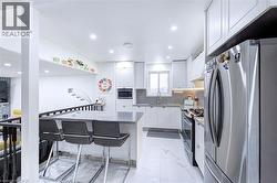 Modern kitchen featuring white shaker cabinetry, stainless steel appliances, a center island with counter seating, recessed lighting, and large format tile flooring - 