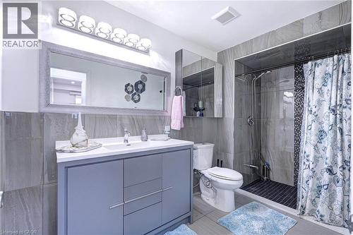Bathroom featuring a gray vanity with an integrated sink, a large framed mirror, and a tiled shower enclosure with dark mosaic accents - 214 Merrilee Crescent, Hamilton, ON 
