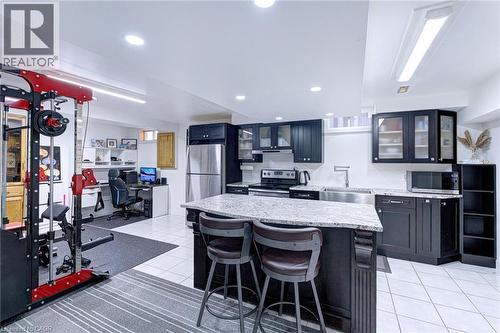 Open-concept lower level featuring a full kitchen with dark cabinetry, stainless steel appliances, and a granite island with seating - 214 Merrilee Crescent, Hamilton, ON 