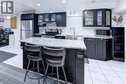 Kitchen featuring dark wood cabinetry, light granite countertops, stainless steel appliances, and white tile flooring - 
