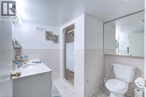 Bathroom featuring a vanity with an integrated sink, a glass-enclosed shower, a wall-mounted medicine cabinet, and light-toned floor and wall tiling - 214 Merrilee Crescent, Hamilton, ON 