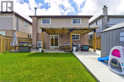 Rear exterior featuring a brick and siding facade, a ground-level concrete patio with a wood pergola, a sliding glass door, and a green lawn area - 214 Merrilee Crescent, Hamilton, ON 