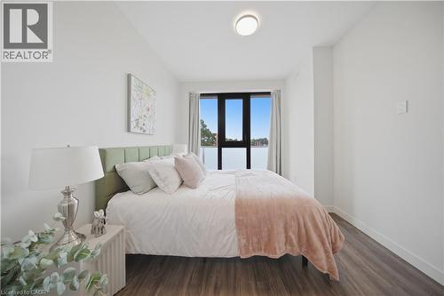 Light-filled bedroom featuring a large window with dark framing and sheer curtains, wood-finish flooring, and a modern ceiling light fixture - 1055 Weber Street E Unit# 207, Kitchener, ON 