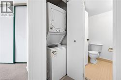 Compact laundry closet featuring a stacked white washer and dryer unit, with a nearby half bathroom including a toilet and beige tiled flooring - 