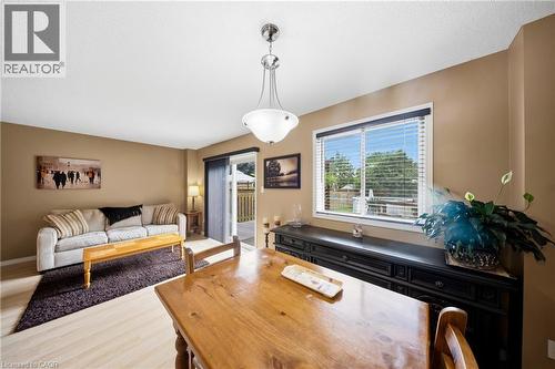 Open-concept living and dining area featuring light wood-finish flooring, neutral-toned walls, a chrome and frosted glass chandelier, and a large window with blinds overlooking the exterior - 16 Scottacres Boulevard, Caledonia, ON 