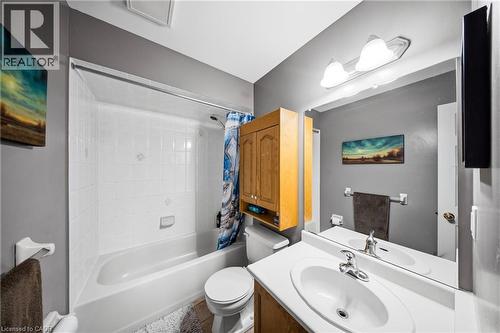 Bathroom featuring a white tub and shower combination with white tiled surround, a light wood-finish vanity with an integrated white sink, a wall-mounted medicine cabinet, and overhead vanity lighting - 16 Scottacres Boulevard, Caledonia, ON 