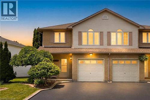 Two-story property featuring a brick and siding exterior, two garage doors with window inserts, and arched top-floor windows - 16 Scottacres Boulevard, Caledonia, ON 