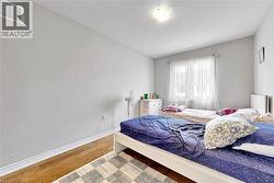 Well-lit interior space featuring wood-finish flooring, white baseboards, and a window with sheer curtains - 