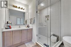 Contemporary bathroom featuring a glass-enclosed shower with a tiled niche, a single vanity with a white countertop, and a large mirror with a four-bulb vanity light - 