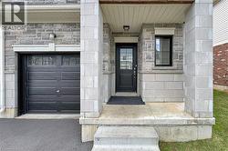 Stone veneer facade with a covered entry, black paneled garage door with upper window inserts, and concrete porch - 