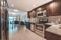 Kitchen featuring dark wood cabinetry, stainless steel appliances, speckled granite countertops, and a complementary backsplash - 