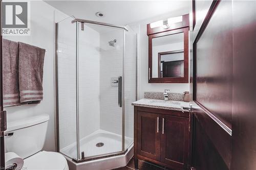 Compact bathroom featuring a corner glass-enclosed shower, a white subway tile surround, a dark wood-finish vanity with a stone countertop, and a coordinating framed mirror with integrated lighting - 1235 Richmond Street Unit# 1406, London, ON 
